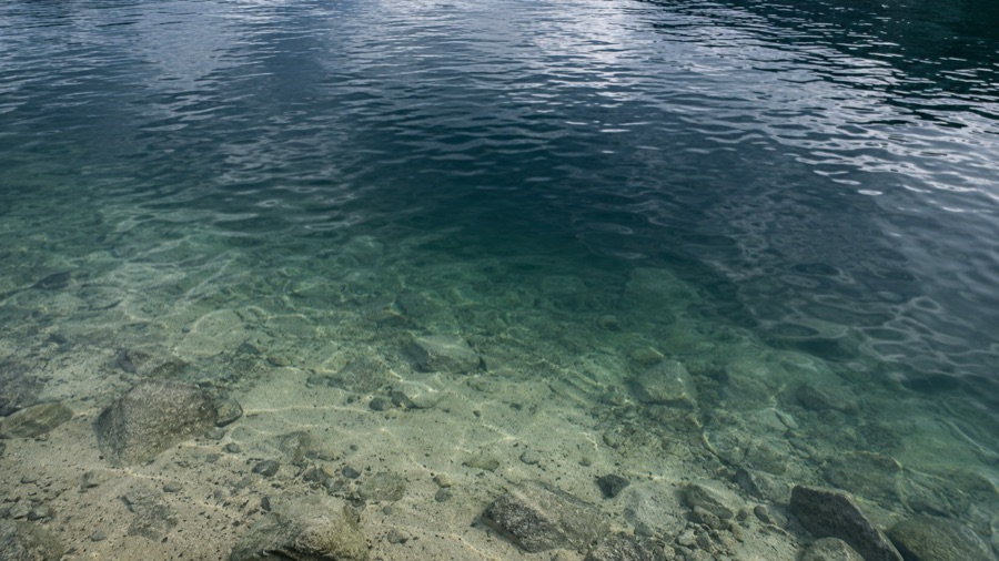 Calm lake water turning from a shallow sandy bottom toward deeper water