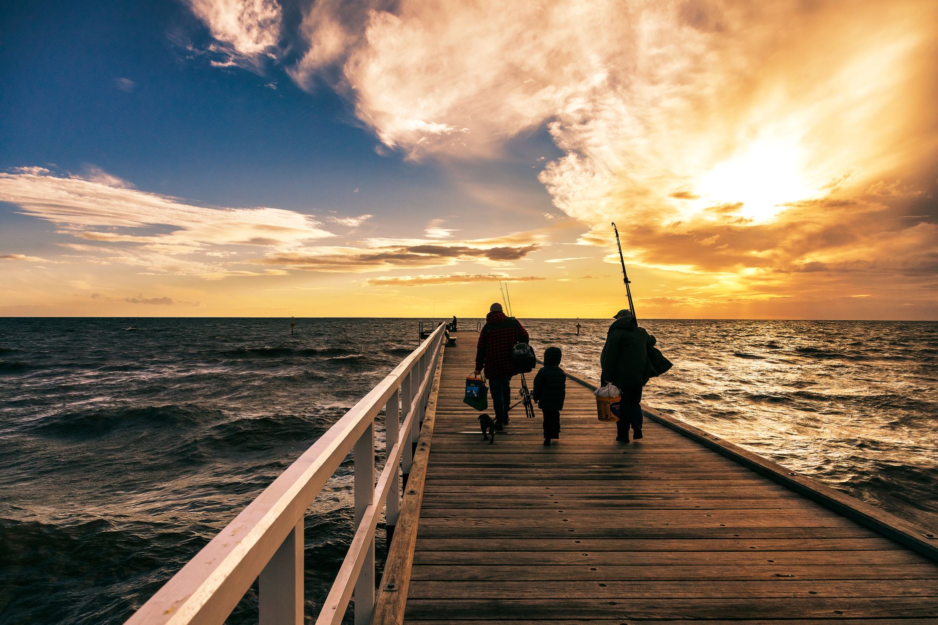 Angler fishing from a wooden pier at golden hour with ocean waves below and clear sky