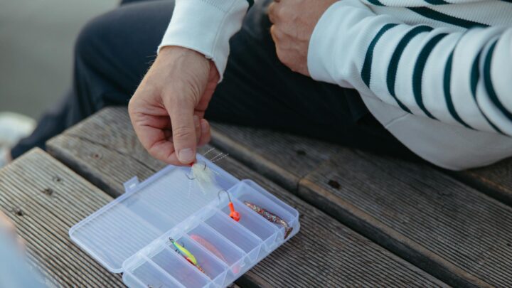 Beginner angler choosing a fishing lure from an open tackle box at a lake at dawn