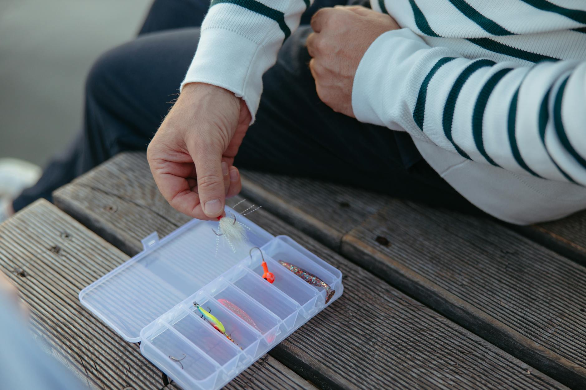 Beginner angler choosing a fishing lure from an open tackle box at a lake at dawn