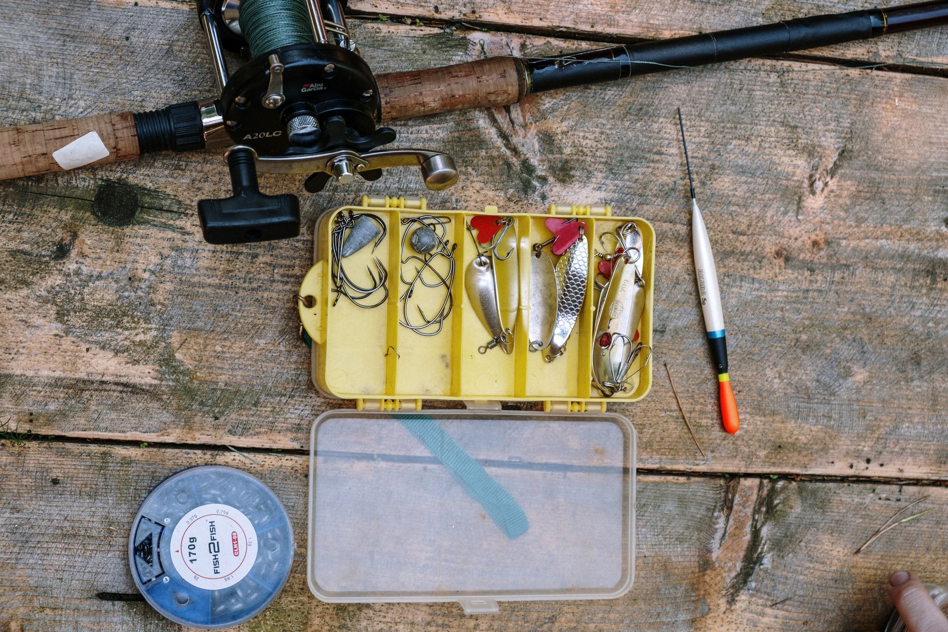 Starter fishing gear laid out on a surface including spinning rod, reel, tackle box, and bait supplies.