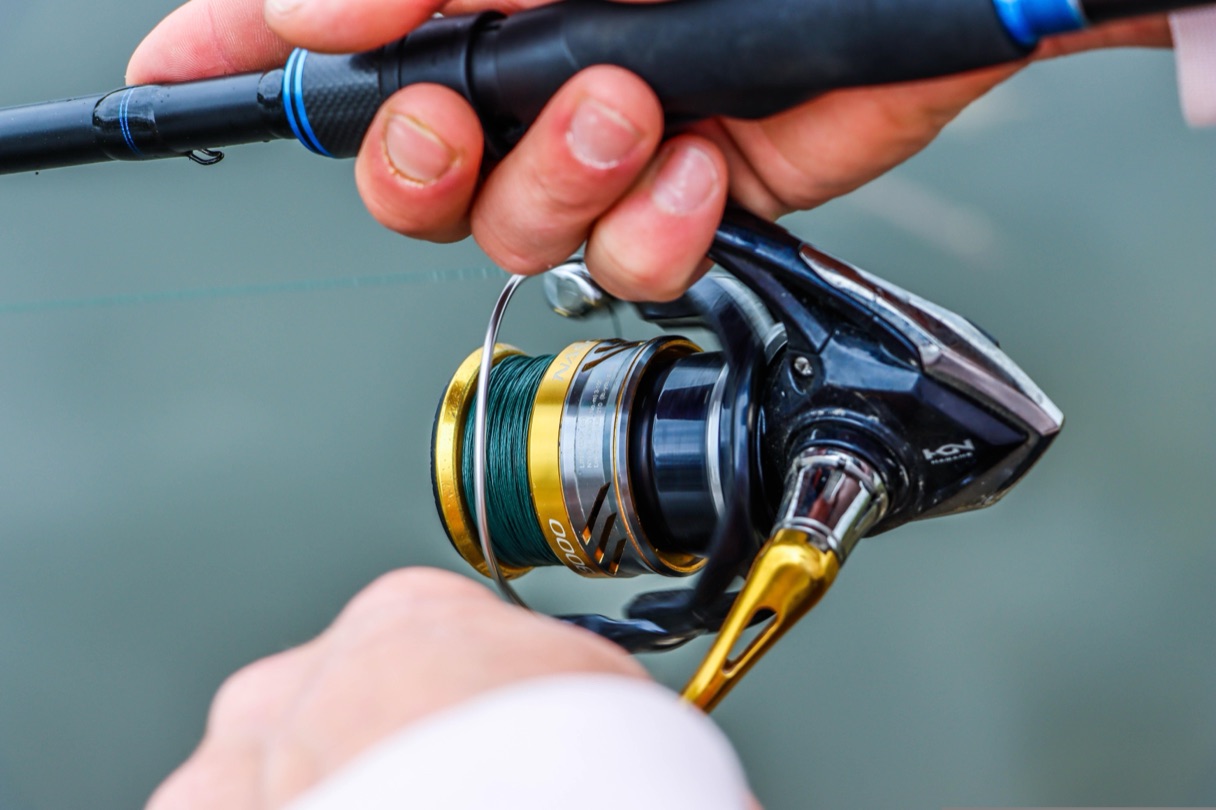 Angler's hands gripping a spinning reel and rod with water in the background