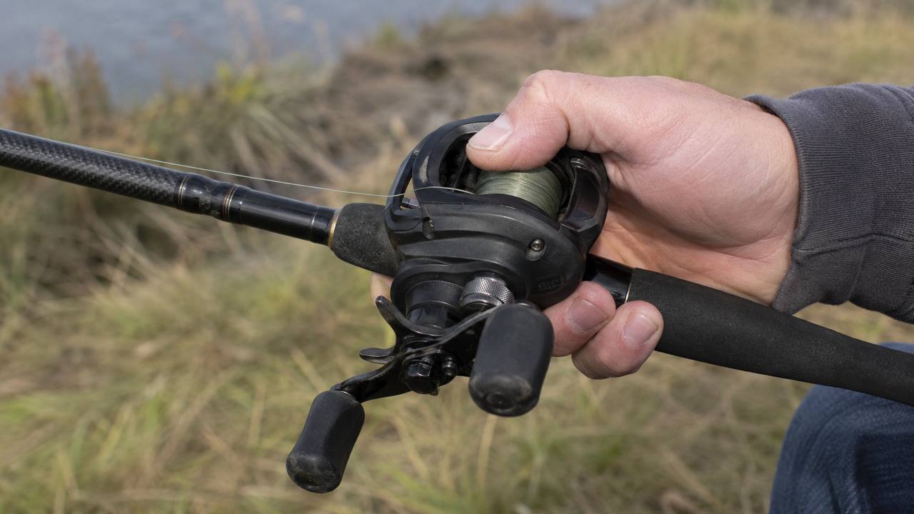 Baitcasting reel mounted on top of a fishing rod showing the revolving spool and thumb control area
