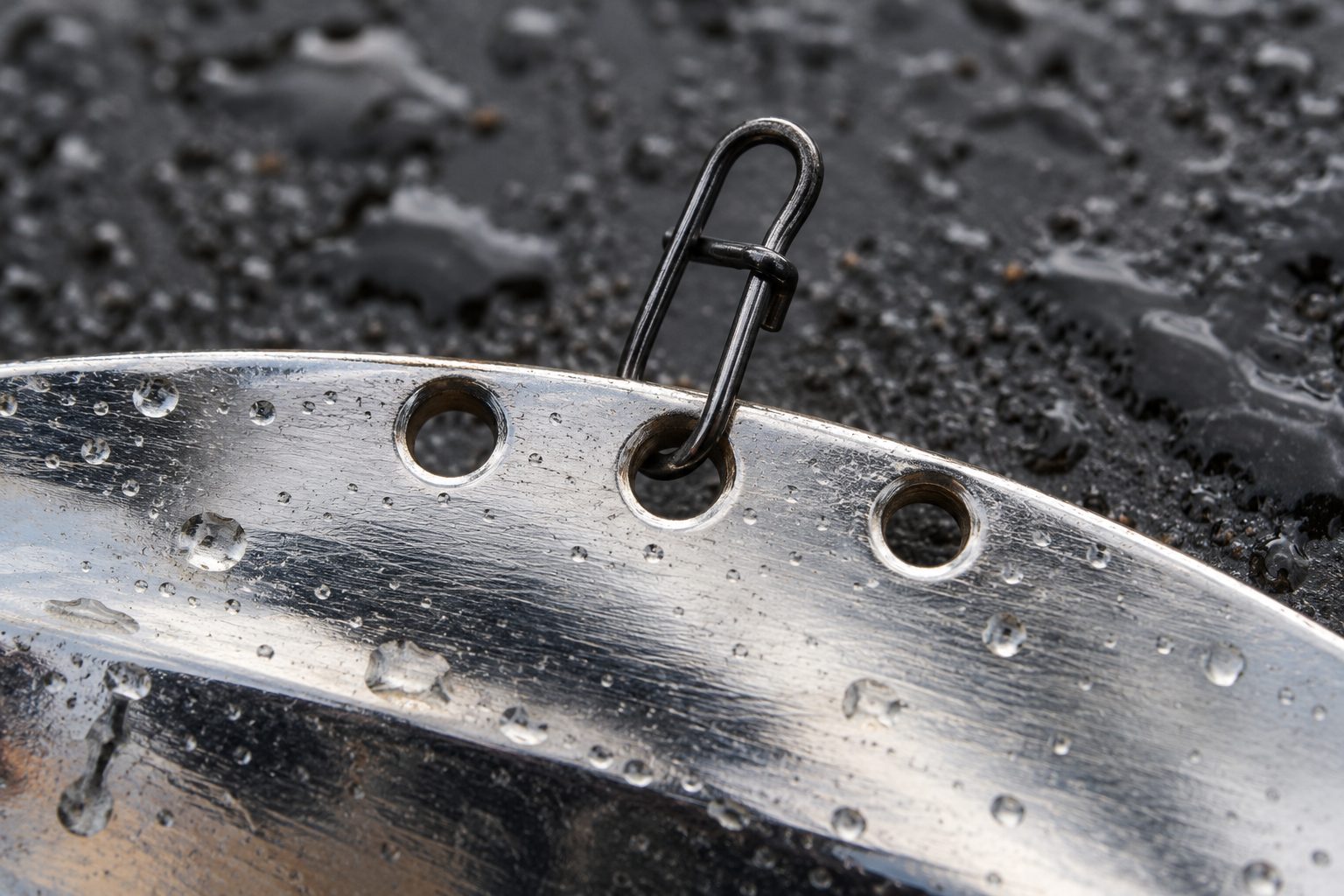 Close-up of the three line-tie holes along a metal blade bait's spine with a snap in the middle hole
